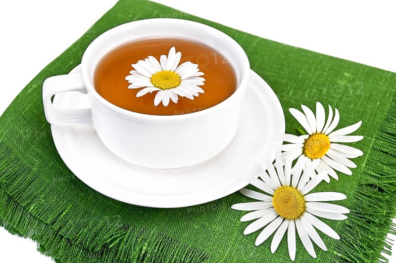 Herbal tea in a white cup with daisies on the green napkin, isolated on a white background