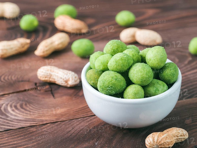Peanut snack for beer, wine, party bar. Salted peanuts in green vasabi glaze on brown wooden table. Copy space