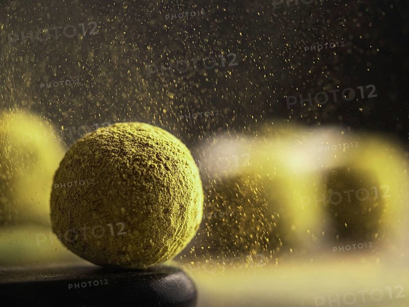 Homemade truffles candy with matcha tea powder in green tea dust cloud over dark background. Copy space right for text or design, banner. Shallow depth of field