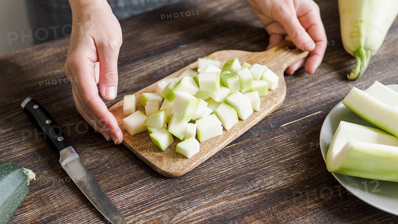 Zucchini harvest. Woman slices zucchini cubes for freezing on wooden table. Farm organic zucchini harvesting