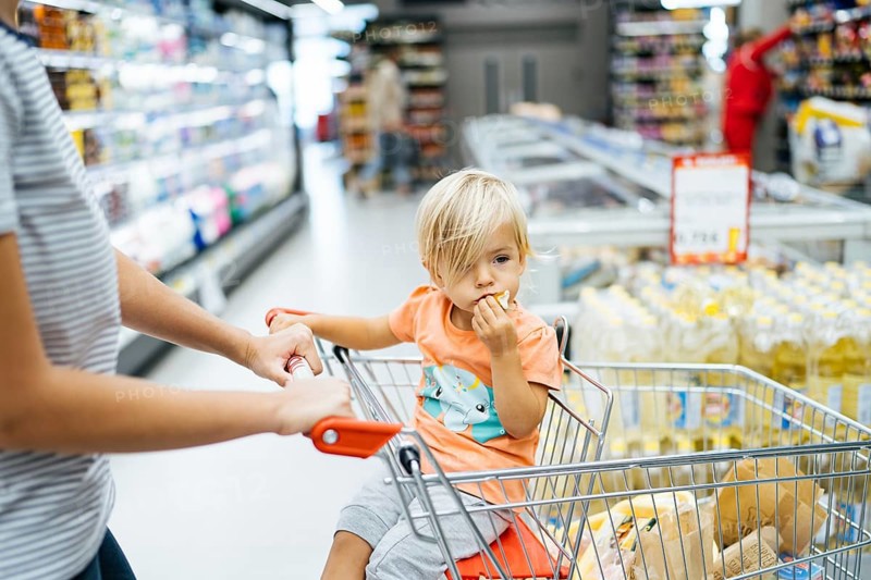 Budva, Montenegro - 17 march 2021: A child sits in a trolley in a supermarket and eats a bun