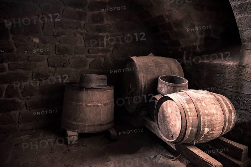 Vintage image with the interior of a stone wine cellar and aged wooden barrels, in low light. Perfect background or frame for a country life concept or medieval way of making wine