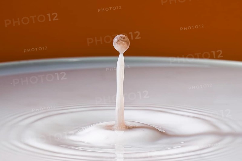 Single dripping water jet hits smooth surface in front of orange background, water droplets, collision, highspeed photography, concept, water figures