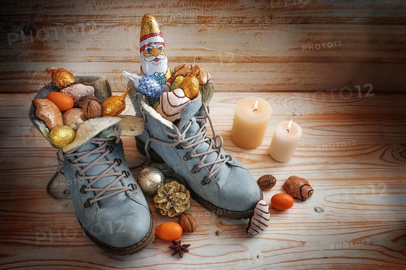 Boots filled with sweets, chocolate Santa and Christmas decoration on a wooden background with candles, tradition on German Nikolaus Tag meaning Nicholas day, copy space