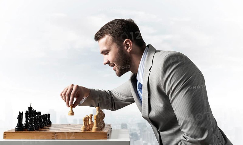 Concentrated businessman playing chess game. Successful management and leadership concept. Confident young man in business suit sitting at desk with chess. Operative tactics and strategy planning