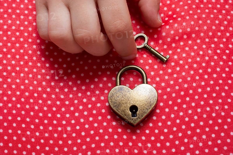 Hand holding a heart shaped lock and key on a red background