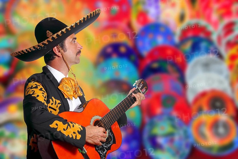 Charro Mariachi playing guitar over colorful blur handcrafts background