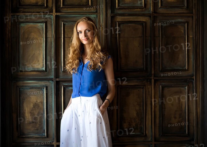 Portrait of the blonde woman in blue blouse staying in front of dark wall and keep smiling