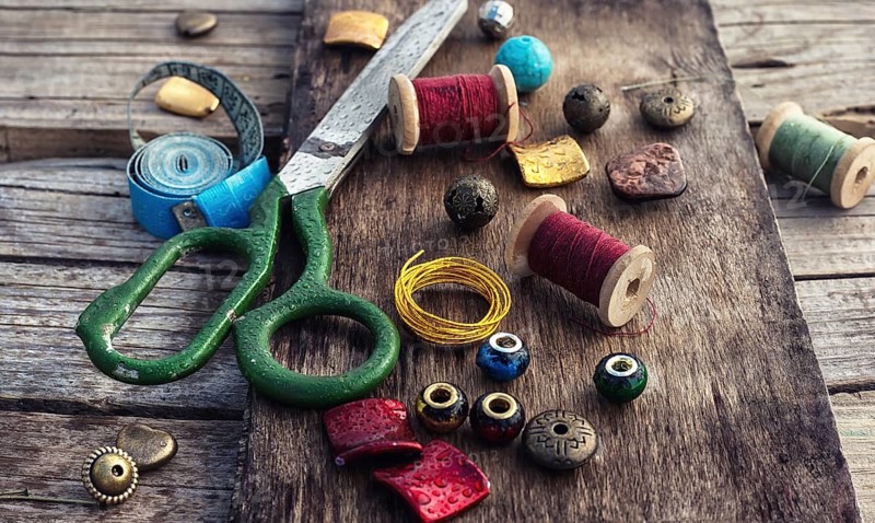 Outdated tools and jewellery for needlework on wooden background