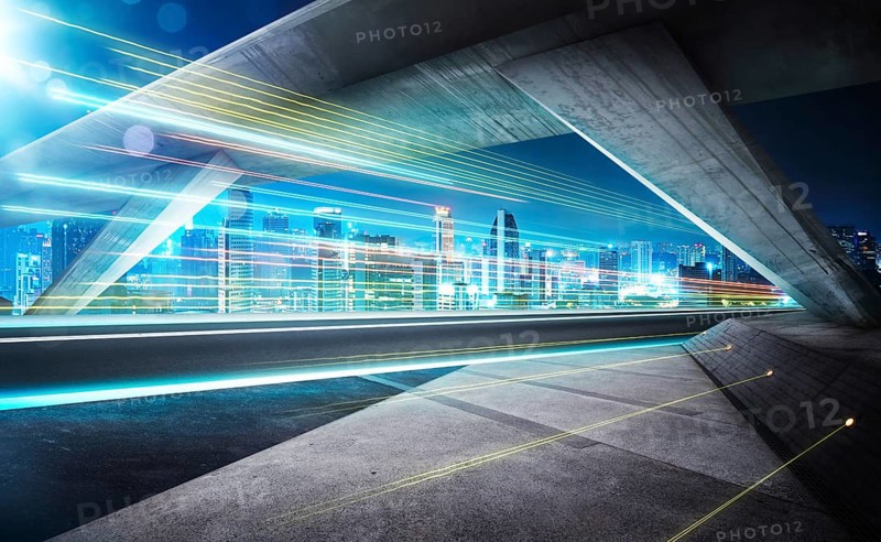 Empty asphalt road under the bridge during the night with light trails and beautiful city skyline background