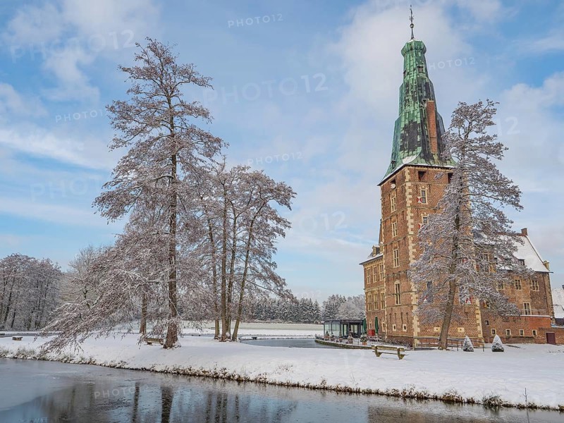 Castle with high tower in winter. Snow-covered trees and a frozen lake in the foreground, Raesfeld, münsterland, germany