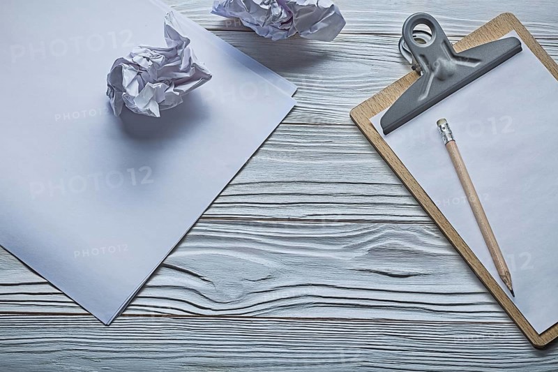 Crumpled paper balls and small clipboard with pencil on vintage white wooden boards
