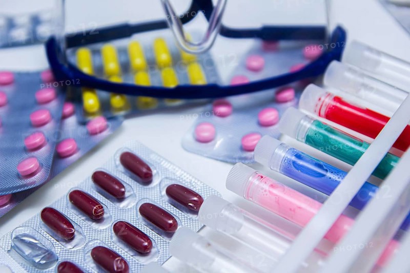 An arrangement of colorful pills and test tubes with safety glasses nearby