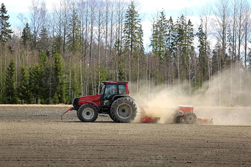 SALO, FINLAND, MAY 7, 2017: Farmer cultivates field with red Valtra tractor and seed drill surrounded by dust on a clear day of spring in South of Finland