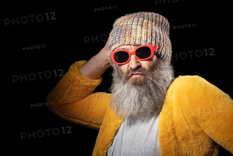 Creative older man with grey beard in fashionable clothes on black background