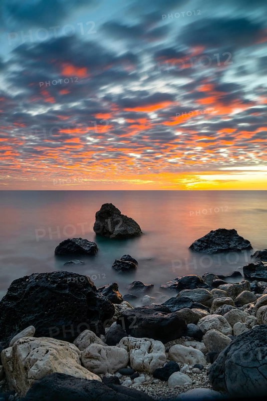 A colorful sunrise at Cala Gonone with black and white rocks and boulders in the foreground