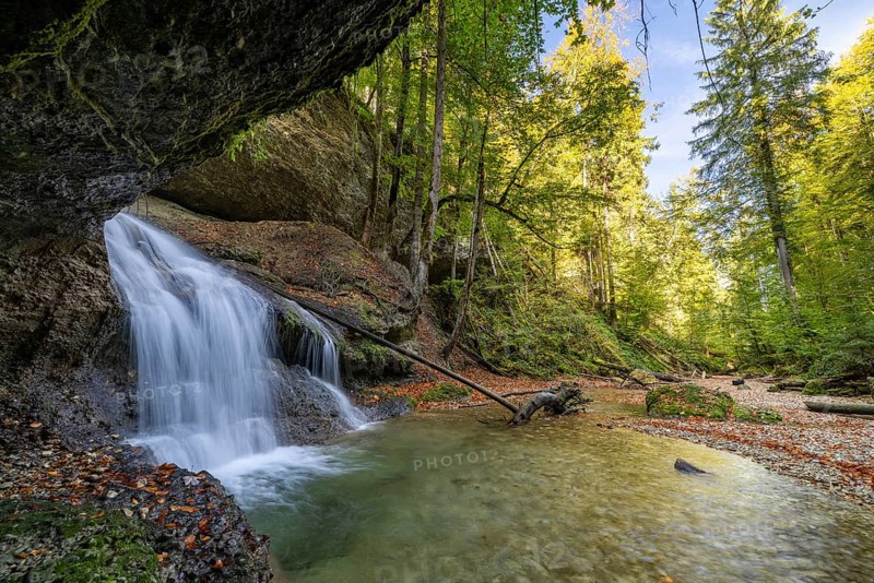 Picturesque waterfall in the middle of a tranquil forest with clear skies and surrounding rocks and trees, Hasenreuter Wasserfall, Scheidegg, Bavaria, Germany, Europe