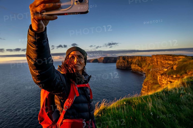 Female hiker taking a selfie, Cliffs of Moher, The Burren, County Clare, Ireland, United Kingdom, Europe