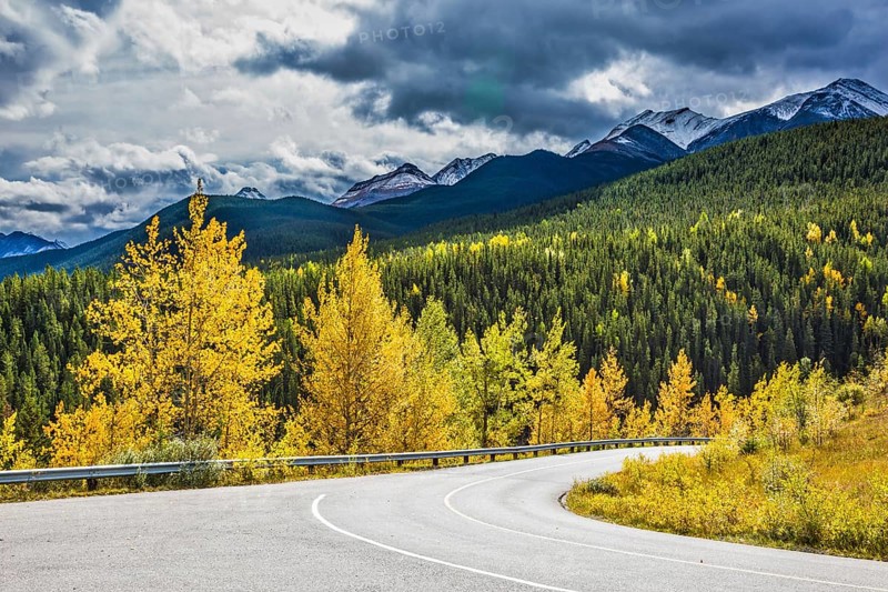 Gorgeous stormy sky in October. Road among autumn forest. Rocky Mountains of Canada