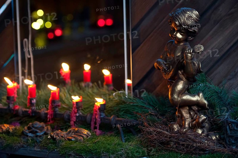A golden angel figure next to a row of burning red candles on moss, borken, münsterland, germany