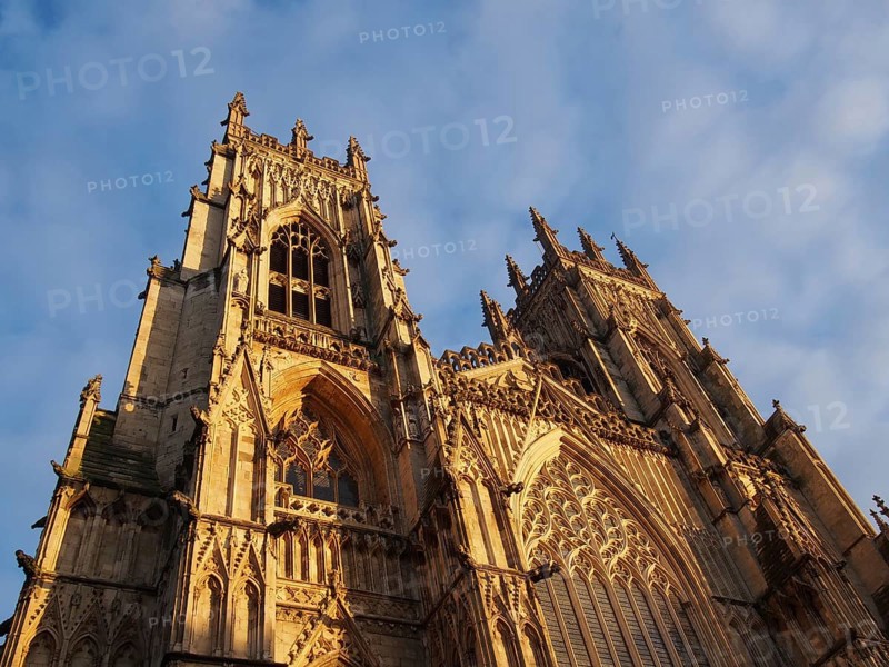 A front view of the towers at the entrance to york minster in sunlight against a blue cloudy sky