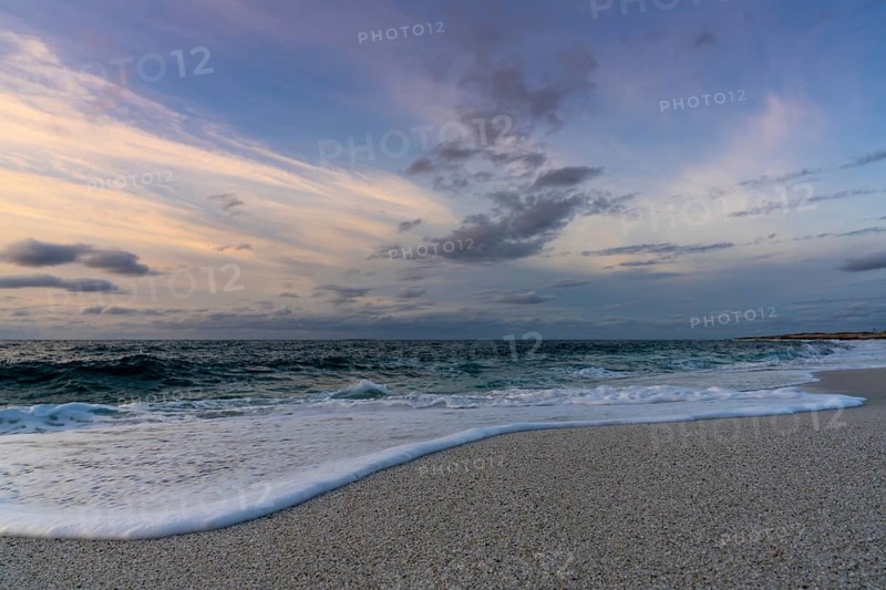 A low angle view of white sand beach with waves rolling in under a colorful sunset sky