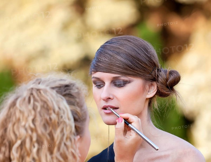 Makeup master applying lipstick with brush on caucasian girl lips