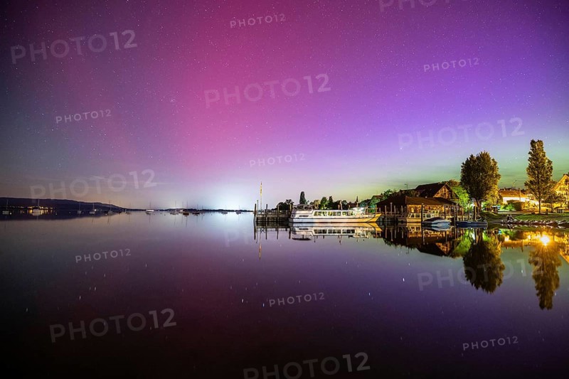 In a calm lake, the vivid northern lights are reflected next to boats and trees, harbour, Allensbach, Lake Constance, Baden-Württemberg, Germany, Europe