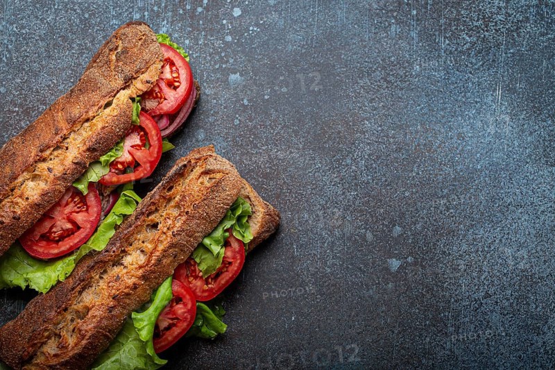 Two dark ciabatta sandwiches with green salad, ripe red tomatoes, onion and tuna on rustic concrete stone background top view. Vegetable vegetarian sandwiches, healthy snack or lunch. Space for text, food photography