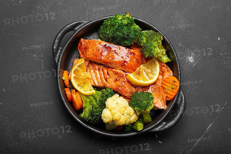 Healthy baked fish salmon steaks, broccoli, cauliflower, carrot in cast iron casserole bowl black dark stone background. Cooking a delicious low carb dinner, healthy nutrition, food photography