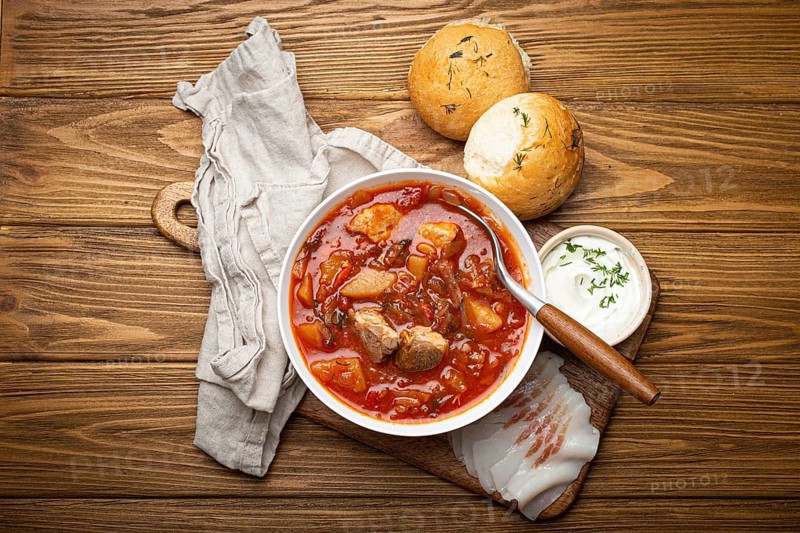 Ukrainian Borscht, red beetroot soup with meat, in white bowl with sour cream, garlic buns Pampushka and salo slices on rustic stone background. Traditional authentic dish of Ukraine, food photography, food photography