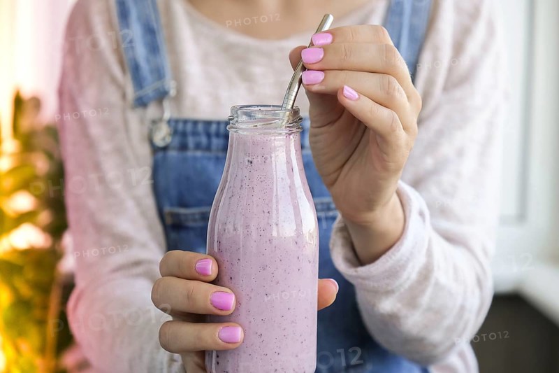 Female hands holding Blueberry smoothie topped with blueberries. Woman eating glass of breakfast protein smoothie drink made from pureed raw blueberries, banana, milk, yogurt, and cottage cheese. Vegetarian vegan food