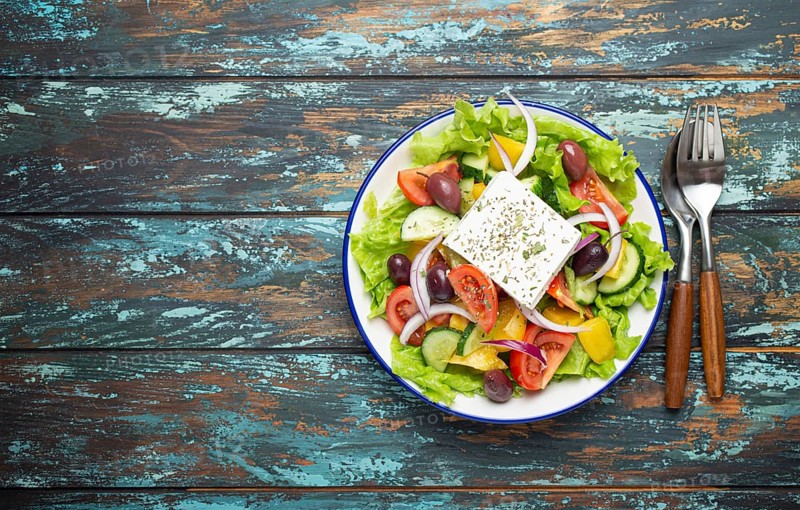 Traditional Greek Salad with Feta Cheese, Tomatoes, Bell Pepper, Cucumbers, Olives, Herbs in white ceramic bowl on blue rustic wooden table background from above, Cuisine of Greece. Space for text, food photography, food photography