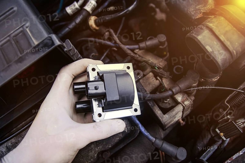 Hand holds car part with engine components around, highlighted by warm lighting