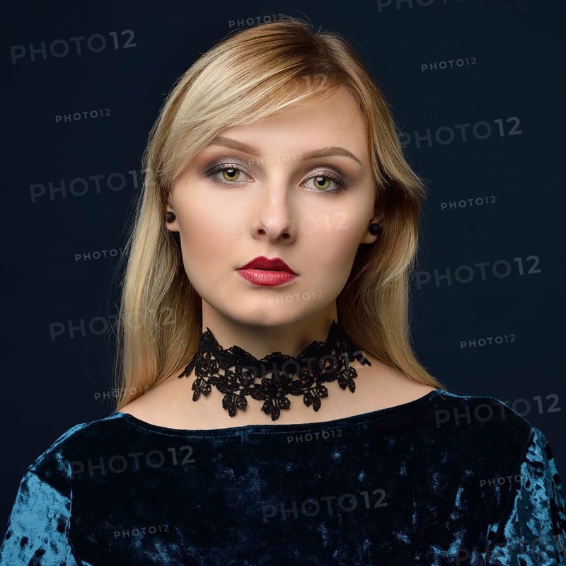 Portrait of the beautiful blonde woman in the blue velvet dress. Shooting in the studio with a dark background