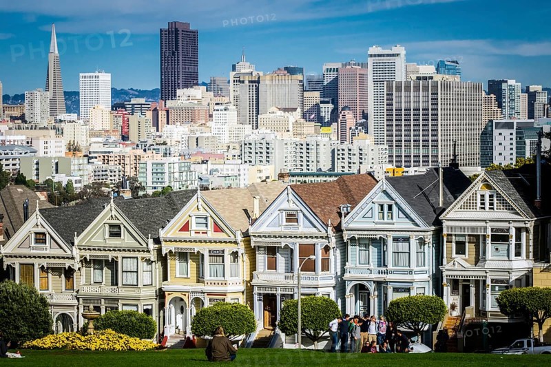 San Francisco, California, United States, November 2013: View on the Painted Ladies Victorian houses of San Francisco with cityscape and skyline in the background on a blue sky. People sitting front, North America