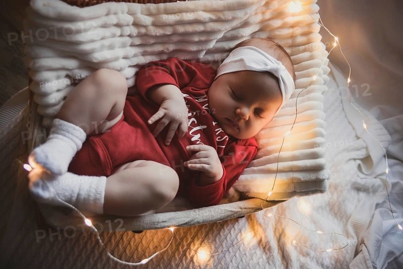 A cute newborn baby in xmas clothes sleeping in a basket on the floor against a Christmas decoration. New Year's Eve