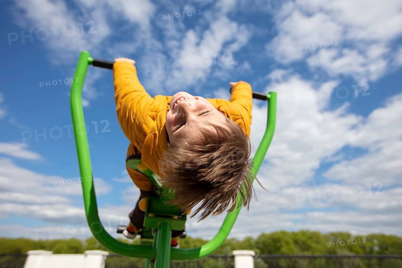 Funny little boy on a swing with his head down. Happy child on a walk. Ten year old boy against the background of the sky