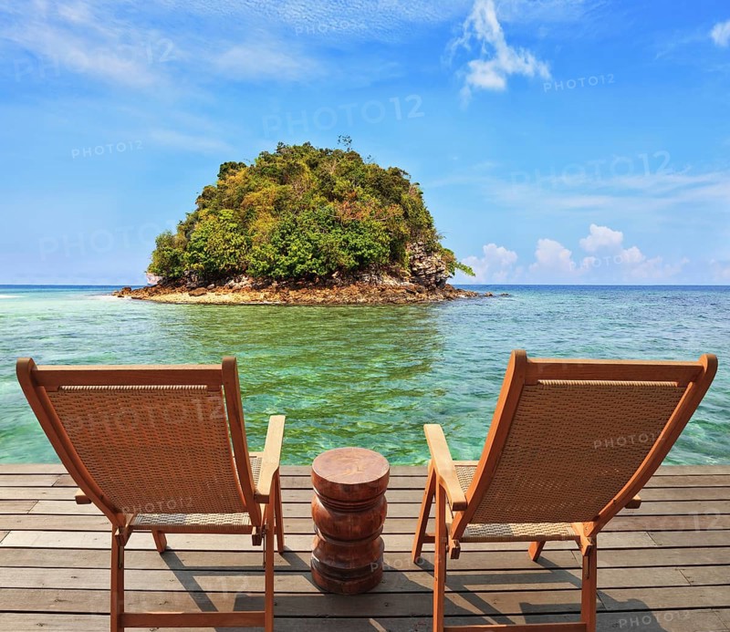 The charming landscape. A green island in a sea bay with emerald water. Two wooden chairs - on a wooden platform. The comfortable place to enjoy the beauty of the landscape