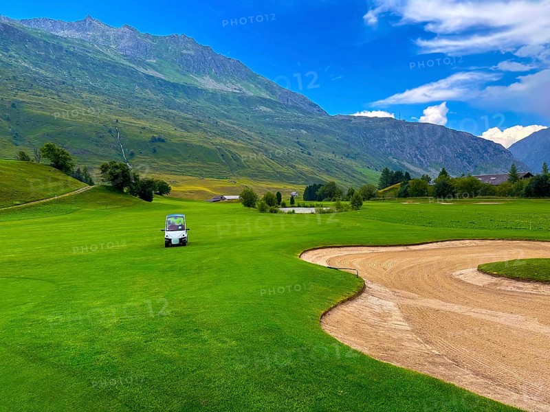 Beautiful Modern Luxury Golf Cart on Golf Course with Sand Trap and with Mountain View in the Swiss Alps in a Sunny Summer Day in Andermatt, Uri, Switzerland, Europe
