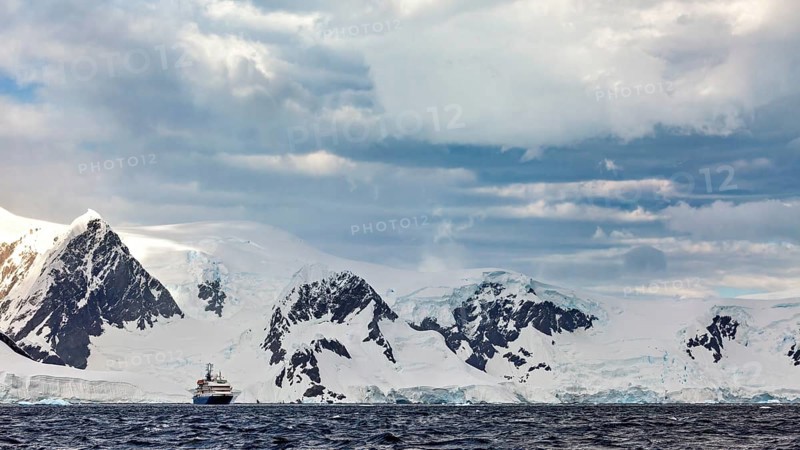 A ship in front of a snow-covered mountain range in a cold, cloudy Antarctic scenery, cruise ship in the Southern Ocean in Antarctica