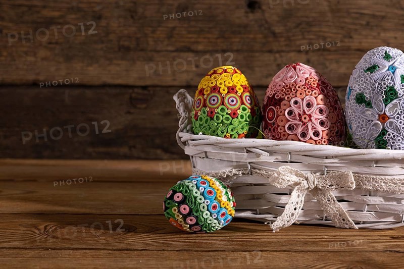 On a background of brown boards set a woven basket with colorful Easter eggs. Easter composition as decoration and symbol of the holiday