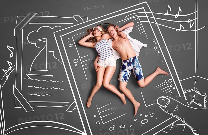 Happy valentines love story concept of a picture of a romantic couple, sharing headphones and listening to the music against chalk drawings background of a photo book