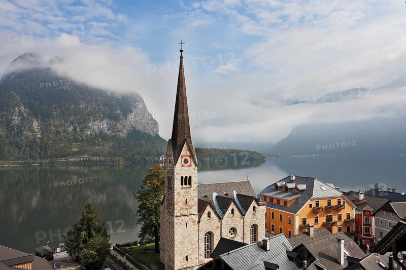The most picturesque small town in Austria - Hallstatt. Slender belfry and Lutheran church on the shore of Lake Hallstatt. On the opposite shore of the lake - the beautiful mountains overgrown with forests