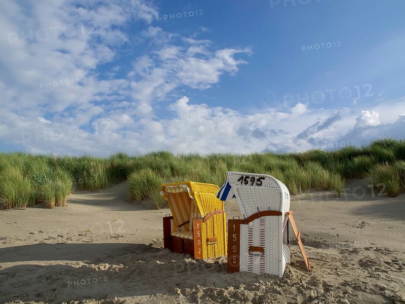 Two beach chairs, yellow and white, on a sunny sandy beach with grassy dunes and blue sky, juist, east frisia, germany