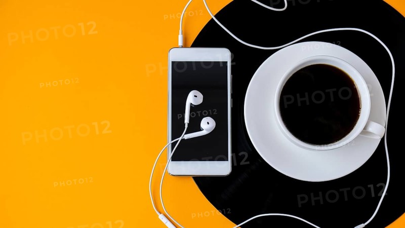 Cup of black coffee on vynil record. Copy space. Listening to music. Retro style. Podcast. Mobile phone with headphones