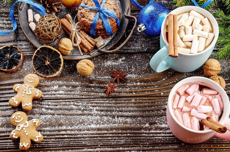 Flat lay Christmas background of two mugs of hot chocolate with marshmallows, spruce branch and tray with gingerbread man cookies on wooden table