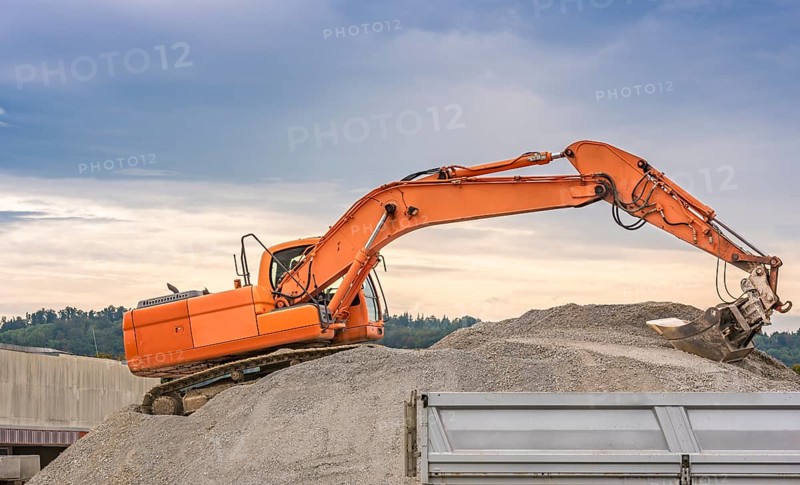 Orange excavator, climbed on a ballast pile, loading material in a trailer