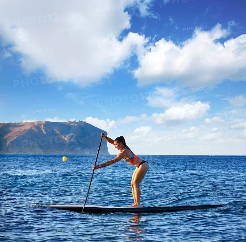 SUP Stand up Surf girl with paddle in a blue ocean sea