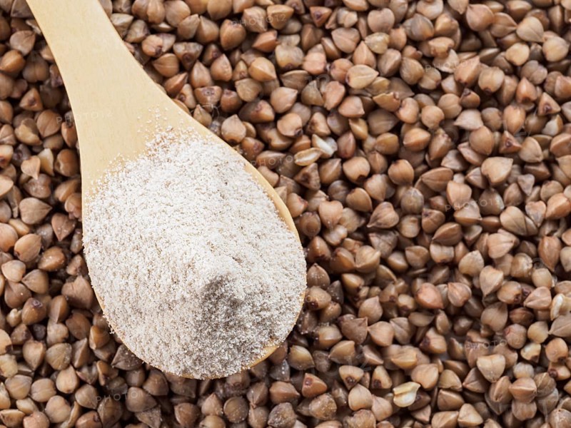 Buckwheat flour in wooden spoon and buckwheat grains. Whole-grain buckwheat flour on buckwheat grains background. Copy space. Top view or flat lay